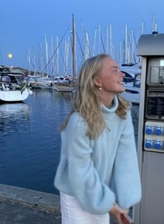 a woman standing next to a parking meter near the water with boats in the background