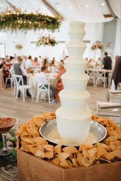 a tall white cake sitting on top of a wooden box filled with chips next to other food