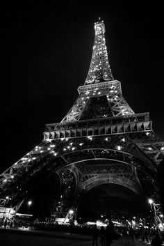 the eiffel tower lit up at night in black and white with people walking around