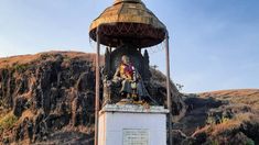 a statue on top of a white pedestal in front of a mountain side with a sky background