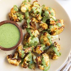 a white plate topped with fried cauliflower next to a cup of green liquid