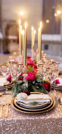 the table is set with gold plates, silverware and pink flowers on top of it