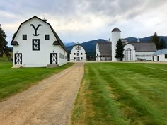 a large white barn sitting on top of a lush green field next to a dirt road