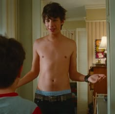 a shirtless young man standing next to a little boy in a living room with his hands out