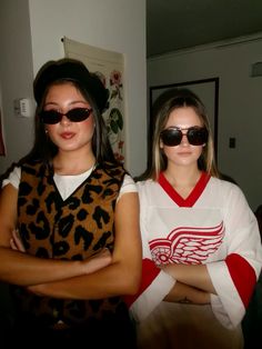 two women wearing sunglasses and sweaters standing next to each other