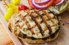 a grilled burger with lettuce, tomato and onion on a wooden cutting board