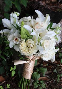 a bridal bouquet with white flowers and greenery on the ground next to leaves