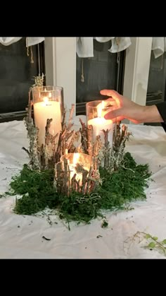 someone is lighting candles in the center of a table with moss and branches on it