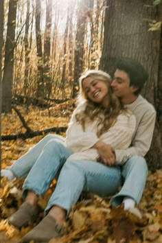 a man and woman sitting next to each other in the woods with leaves on the ground