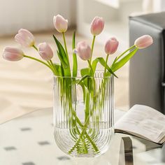 pink tulips in a glass vase on a table next to an open book