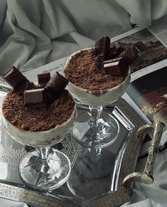 two desserts are sitting on a silver tray next to an open book and magazine