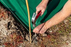 a man holding a pair of pliers in his hand next to a green tarp