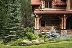 a log cabin sits in the middle of a lush green yard with rocks and trees