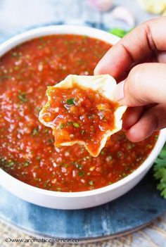 a hand holding a tortilla over a bowl of salsa