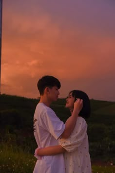 a man and woman standing next to each other in front of a pink sky at sunset