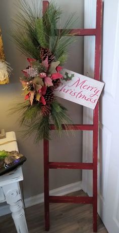 a red ladder decorated with pine cones and greenery next to a merry christmas sign