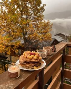 pancakes with fruit are on a wooden table overlooking the mountains and trees in autumn time