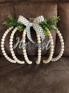 two wreaths made out of wood beads and greenery are sitting on a couch