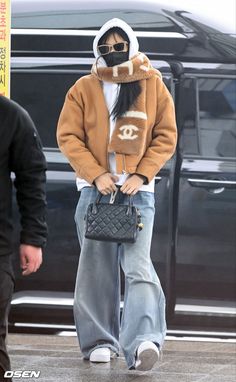 a woman in an oversize jacket and scarf walks down the street with her handbag