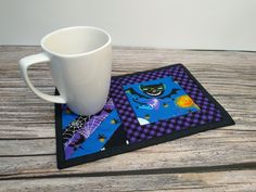 a white coffee cup sitting on top of a wooden table next to a black and purple coaster