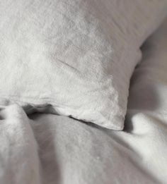 an unmade bed with white linens and pillows on it's side, close up