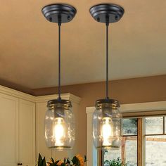 two mason jar lights hanging from the ceiling above a kitchen island with flowers on it