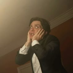 a man in a tuxedo holding his hands to his face and looking up