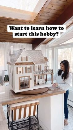 a woman standing in front of a model house on top of a counter next to a window