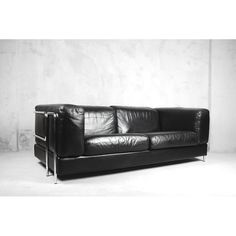 a black leather couch sitting in front of a white wall with a metal frame on it