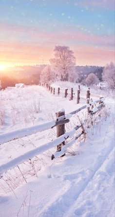 the sun is setting over a snow covered field with a wooden fence in the foreground