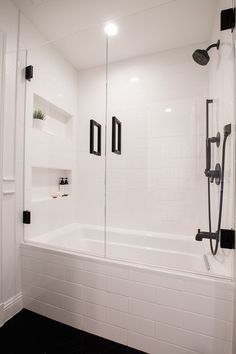 a white bathroom with black accents and tile flooring is pictured in this image, there are two shower heads on either side of the bathtub