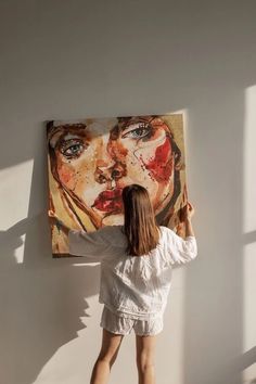 a woman standing in front of a painting on the wall with her hands behind her head