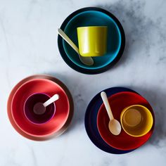 three colorful bowls with spoons on top of them