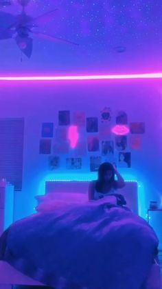 a woman is sitting on her bed in the room with purple lights and pink sheets