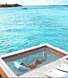 a woman laying in a hammock on top of a wooden dock next to the ocean