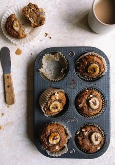 muffins with banana slices and other toppings on a tray next to a cup of coffee