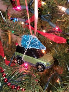 a green car ornament hanging from a christmas tree with red and blue ribbons