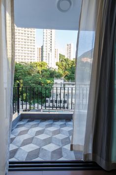 an open balcony with white curtains and black iron railings, looking out onto the city