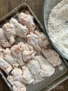 raw chicken and flour in pans on a wooden table next to a glass bowl