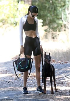 a woman walking her dog on a leash in the woods with no shirt and shorts