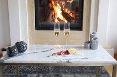 two glasses of wine are sitting on a marble coffee table in front of a fireplace