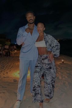 a man and woman standing on top of a beach next to the ocean at night