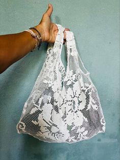 a hand holding a white bag with black and white designs on it, against a blue wall