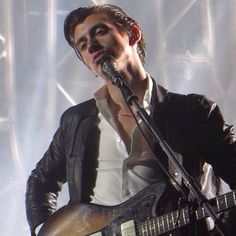 a man holding a guitar and singing into a microphone while standing in front of a stage