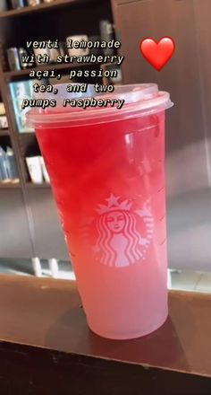 a pink starbucks cup sitting on top of a counter next to a red heart shaped object