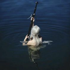 a woman is in the water holding a fishing pole and wearing grey hair with her hands behind her head