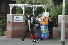 three people walking past a sign that says main entrance and two children with backpacks