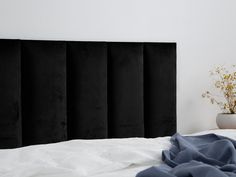 a white bed topped with a black headboard next to a potted plant