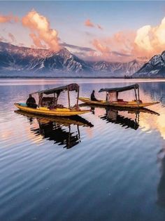 two boats sitting in the middle of a lake with mountains in the backgroud