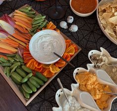 an assortment of dips, chips and vegetables on a table with other food items